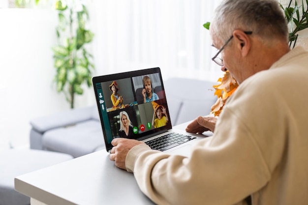 Handsome old man dressed in casual formal style using laptop,\
while sitting on sofa at home. happy grandfather communicate with\
grandchildren. video call concept.