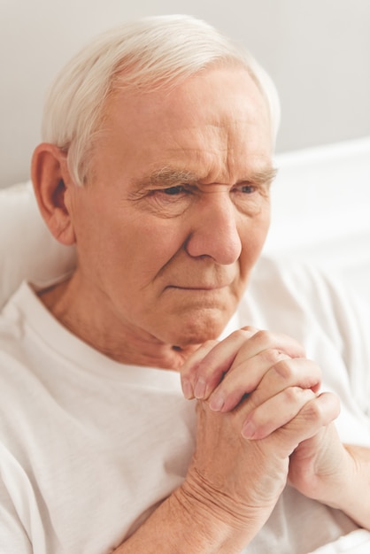 Handsome old man is praying while lying in bed in hospital.