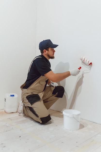 Handsome painter with paint roller in empty room paints the wall