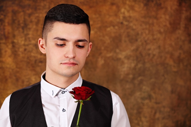 Handsome pensive guy in a black vest with a rose in his hands on valentine's day