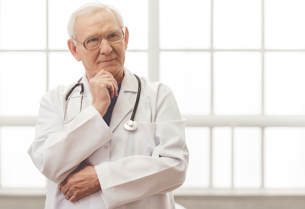 Handsome pensive old doctor in eyeglasses is looking away