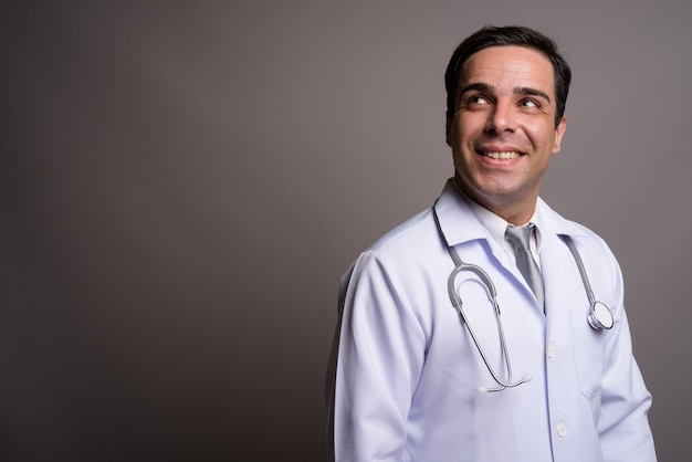 Handsome Persian man doctor against gray wall