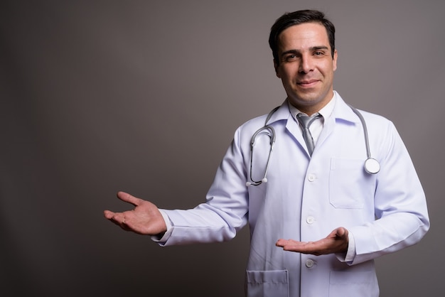 Handsome Persian man doctor against gray wall