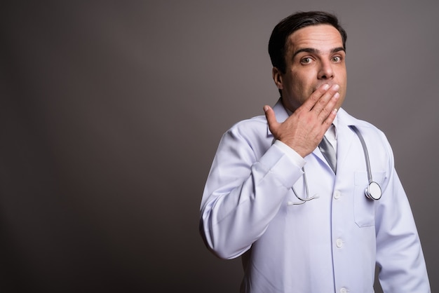 Handsome Persian man doctor against gray wall