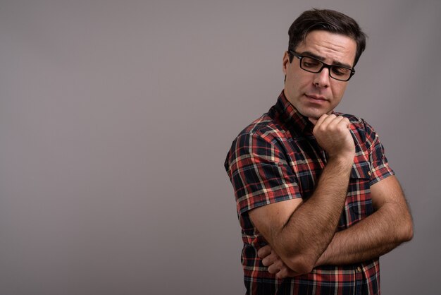 Handsome Persian man wearing eyeglasses against gray wall