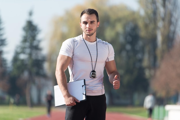 Handsome Personal Trainer With Stopwatch Showing Thumbs Up Sign in City Park Area  Training and Exercising for Endurance  Healthy Lifestyle Concept Outdoor