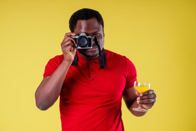 Handsome photographer happy young african man Kenya Africa tourist isolated yellow wall background holding tickets with passport and coctail glass and photo camera trip around the world