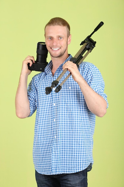 Handsome photographer with camera and tripod on green background