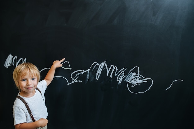 Bel ragazzino giocoso che scrive su una lavagna fingendo di essere un insegnante