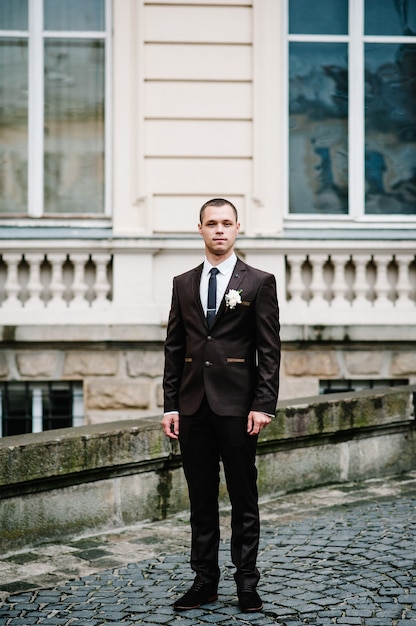 Handsome portrait groom in wedding suit stand on old stone pavement near vintage palace outdoor, old building.