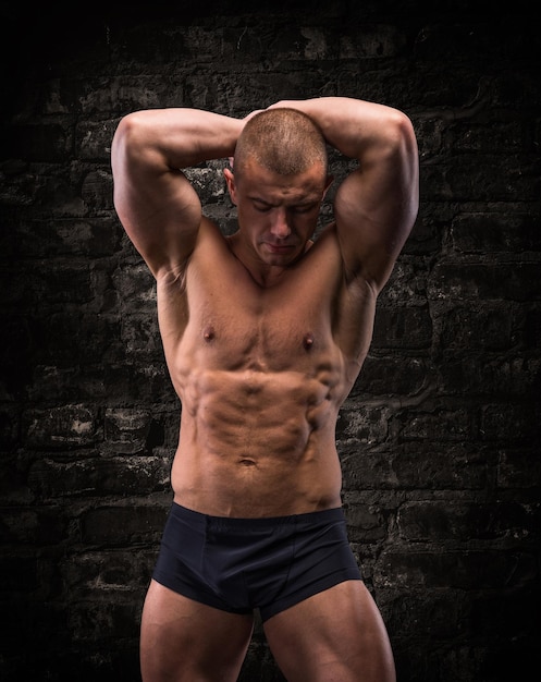 Handsome posing bodybuilder on a background of brick wall