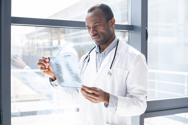 Handsome practitioner looking at roentgen while standing near window