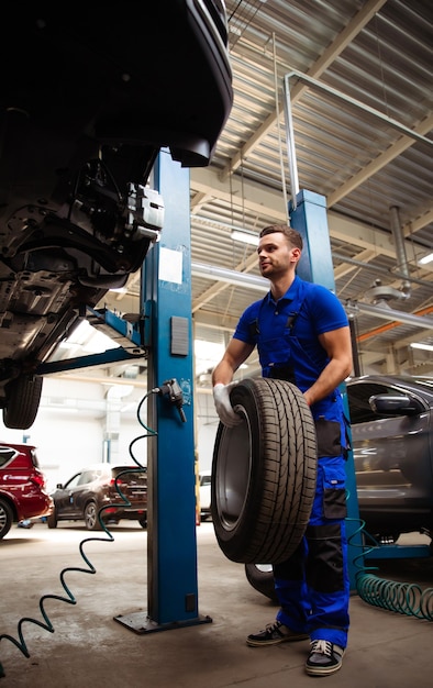 Un bel meccanico professionista cambia una ruota su un'auto o effettua un cambio di pneumatici presso un centro di riparazione auto specializzato