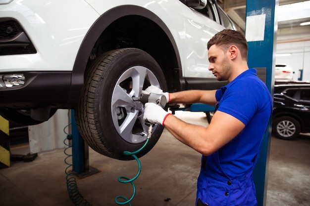 Handsome professional car mechanic changes a wheel on a car or carries out a tire change at a specialized auto repair center