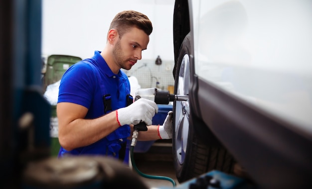 Handsome professional car mechanic changes a wheel on a car or carries out a tire change at a specialized auto repair center