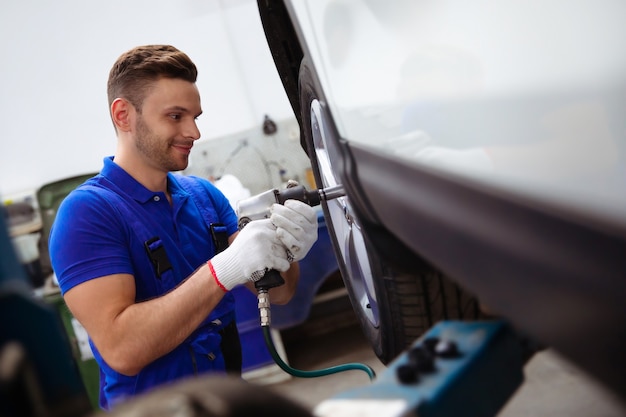 Un bel meccanico professionista cambia una ruota su un'auto o effettua un cambio di pneumatici presso un centro di riparazione auto specializzato