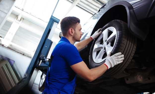 Handsome professional car mechanic changes a wheel on a car or carries out a tire change at a specialized auto repair center