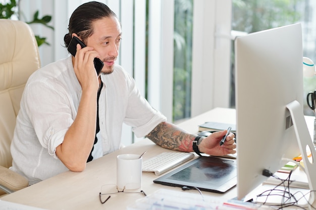 Handsome professional graphic designer talking on phone with client and drawing with digital pen