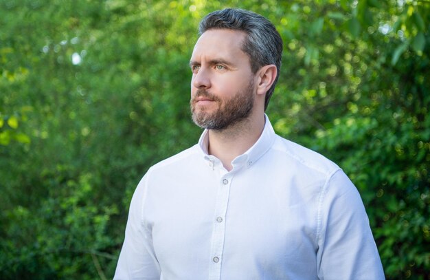 Handsome professional manger in white shirt looking aside natural background