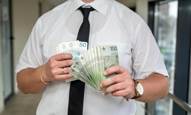 A handsome promising man in a suit and tie holds a large sum of Polish zlotys Business and profit concept