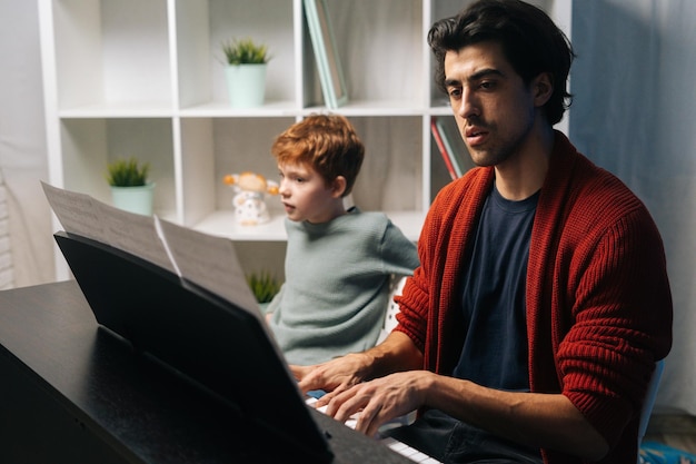 Красивый рыжий мальчик-студент слушает, как его учитель играет на пианино во время урока