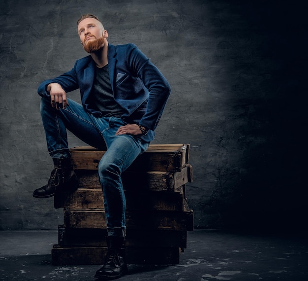 A handsome redhead male dressed in a jeans and a shirt posing on a wooden box.