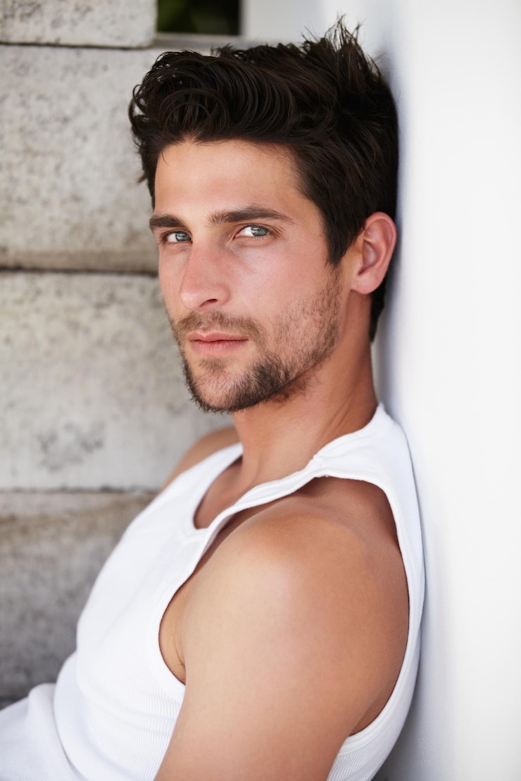 Photo handsome in repose handsome young male staring at you while leaning against a wall