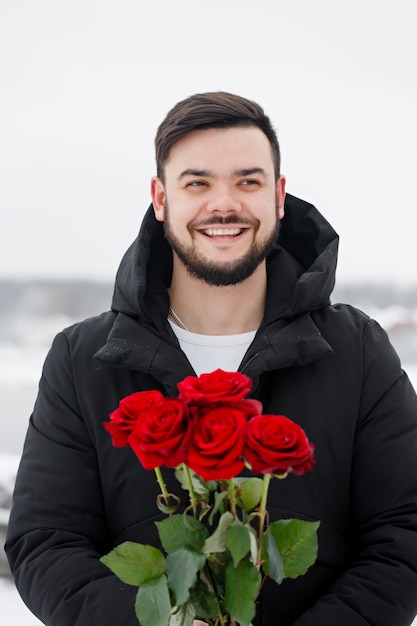 Handsome romantic young man with bouquet of red roses in hands