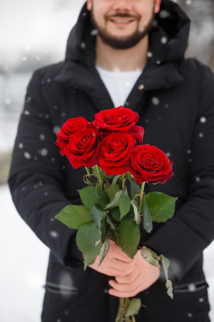 Handsome romantic young man with bouquet of red roses in hands