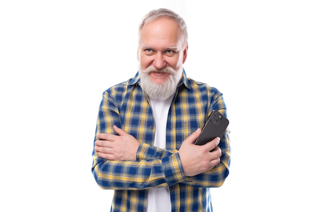 Bell'uomo dai capelli grigi di mezza età con la barba in una camicia con uno smartphone su sfondo bianco