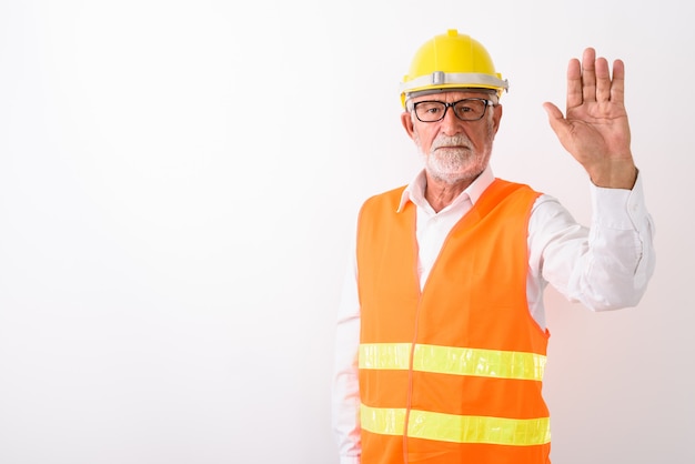 handsome senior bearded man construction worker showing stop hand sign while wearing eyeglasses on white