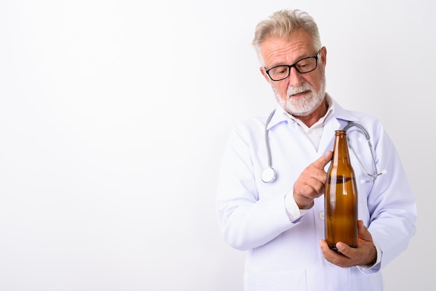 handsome senior bearded man doctor holding and measuring bottle of beer on white