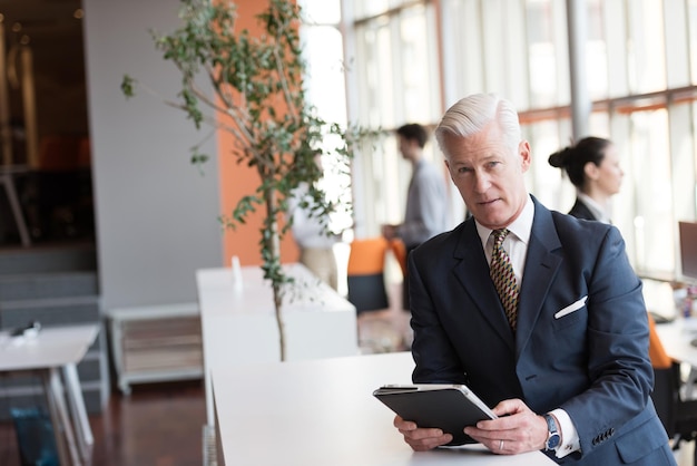 handsome senior business man with grey hair working on tablet computer at modern bright office interior