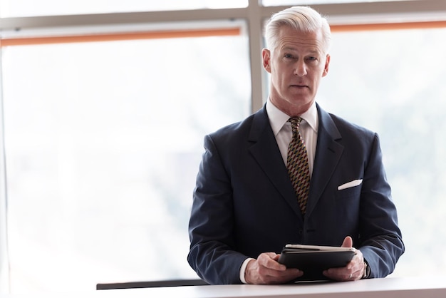 Photo handsome senior business man with grey hair working on tablet computer at modern bright office interior