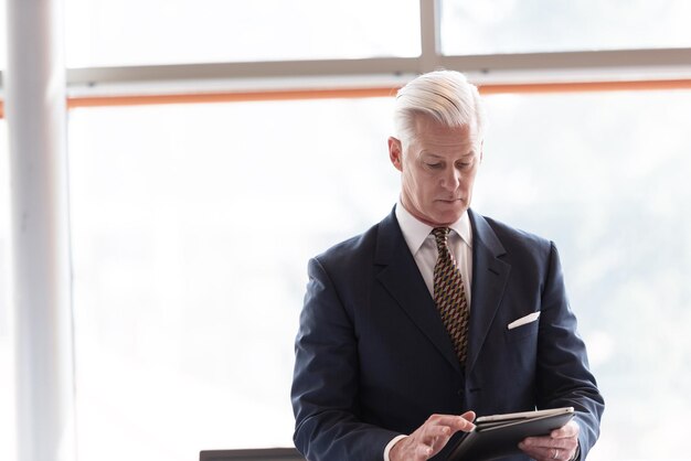 handsome senior business man with grey hair working on tablet computer at modern bright office interior