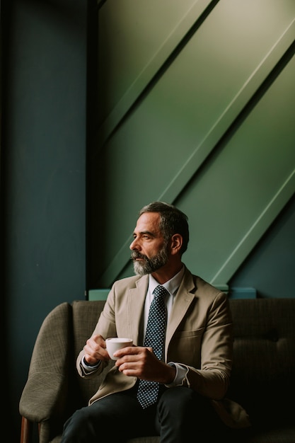 Handsome senior businessman drinking coffee in lobby