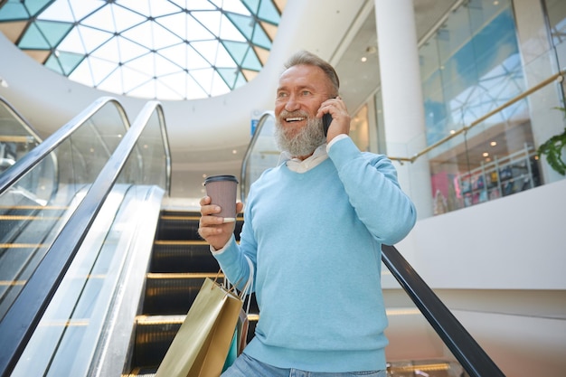 Handsome senior man holding shopping bags talking phone in mall