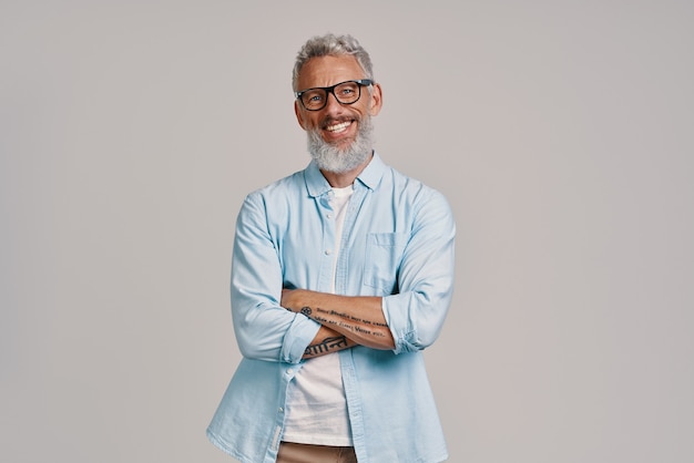 handsome senior man looking at camera and smiling while standing against gray background