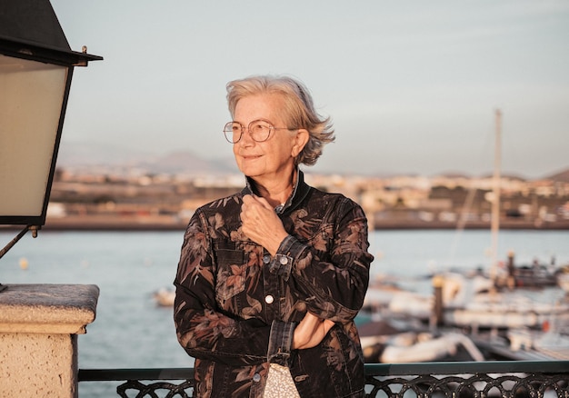 Handsome senior woman at the sea port enjoying free time and\
relax at sunset light elderly caucasian lady on travel or\
retirement