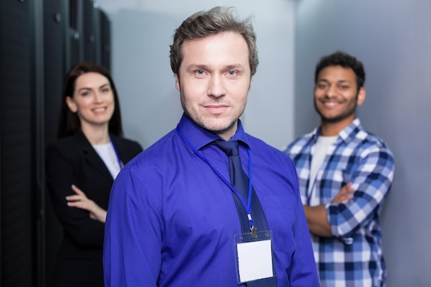 Handsome serious adult man standing in front of his colleagues and looking at you while working in a team