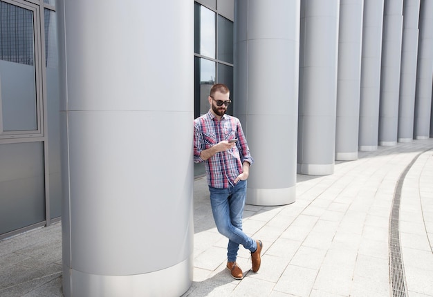 Handsome serious young man with beard in plaid shirt using phone