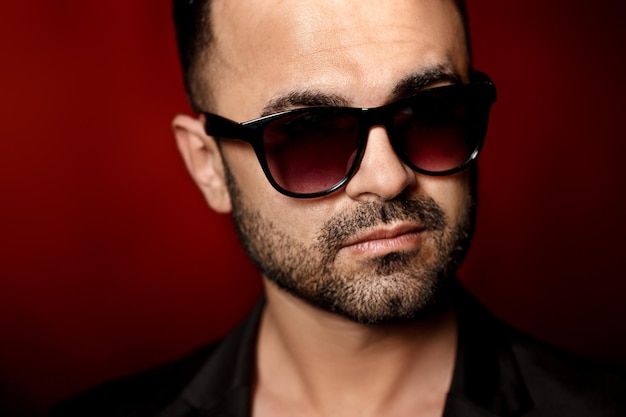 Handsome sexy man in sunglasses and black jacket on red background