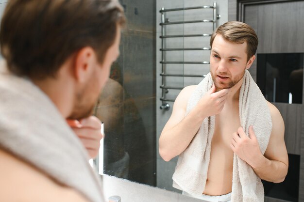 Handsome shirtless man looking in the mirror in the bathroom