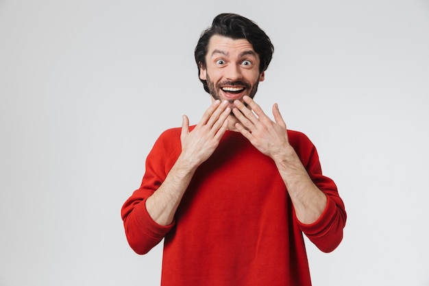 Handsome shocked young bearded brunette man wearing sweater standing isolated over white wall, celebrating