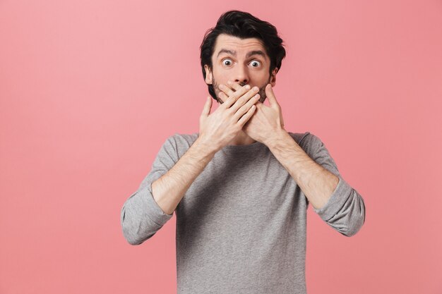 Handsome shocked young bearded brunette man wearing sweater standing over pink, celebrating