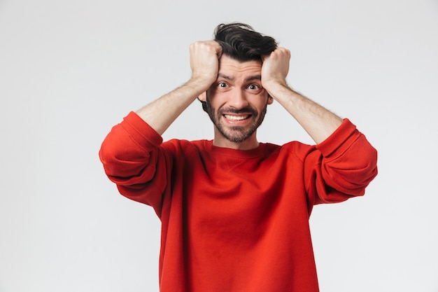 Handsome shocked young bearded brunette man wearing sweater standing over white, celebrating