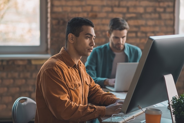 Handsome smart man looking at the computer screen while working as an IT developer