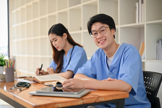 Handsome and smart young Asian male medical student in a uniform studying with his friend