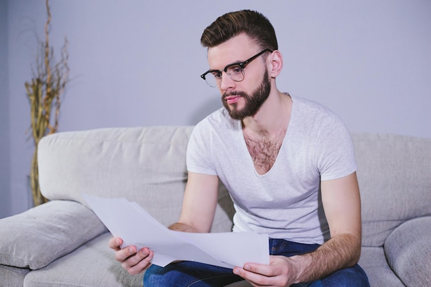 Handsome smiling bearded business man with glasses working with business papers sitting at home on the couch Freelance or work at home