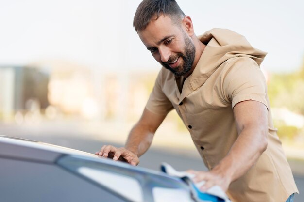 Handsome smiling bearded man cleaning his car using micro fiber cloth. Car washing service concept